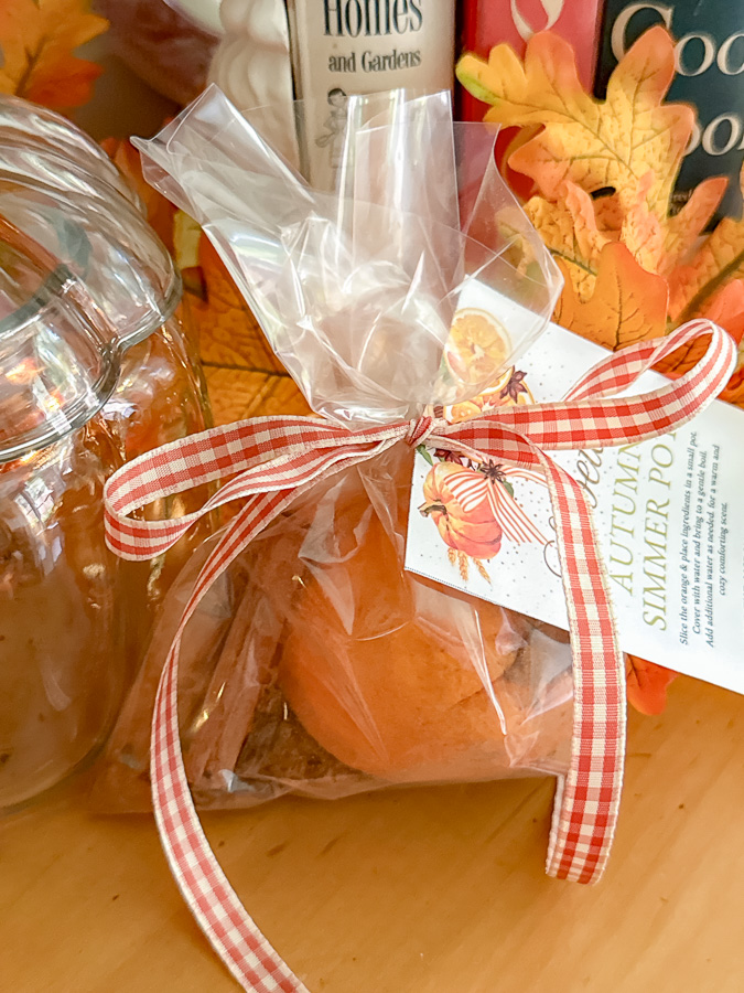 Gingham ribbon tied around a clear bag of ingredients and a autumn simmer pot gift tag added then the ribbon tied into a bow.
