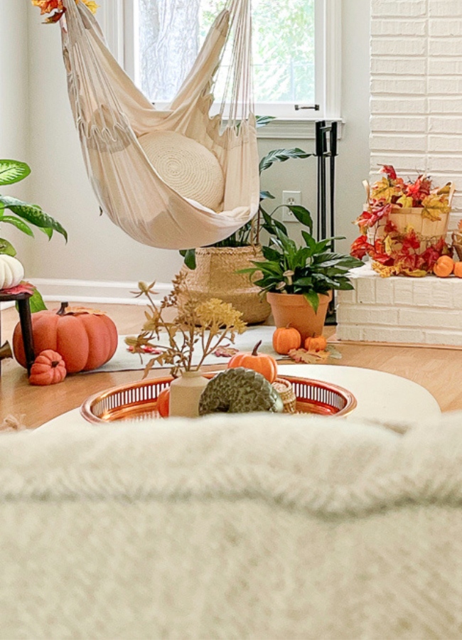 A simple fall tray decor idea. A copper tray on a white coffee table. Inside the tray is a small vase with fall foliage in it. Next to the vase is a stack of wicker coasters with an orange pumpkin on it and next to that is a ceramic acorn.