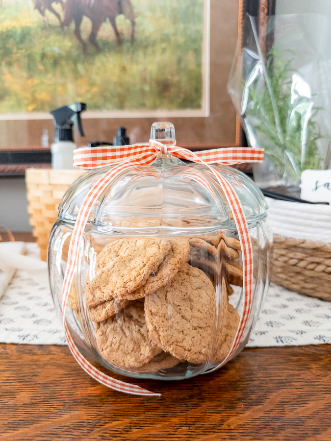 Glass pumpkin cookie jar filled with oatmeal cookies tied with gingham ribbon for a housewarming gift
