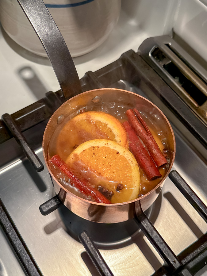 Sliced oranges, cinnamon sticks, whole cloves and dry ingredients in a small copper pot simmering on a stove.