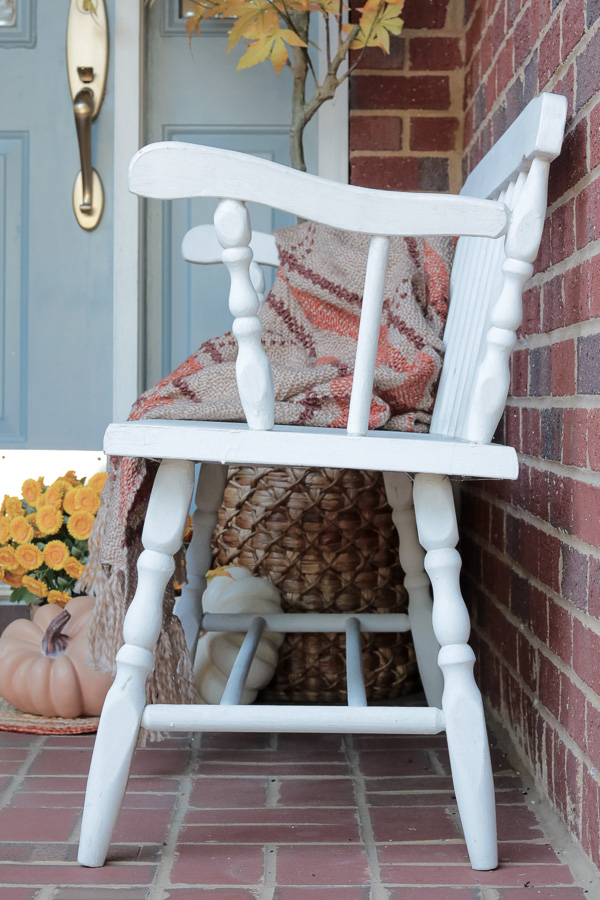 White bench on a porch with a blanket draped over it.