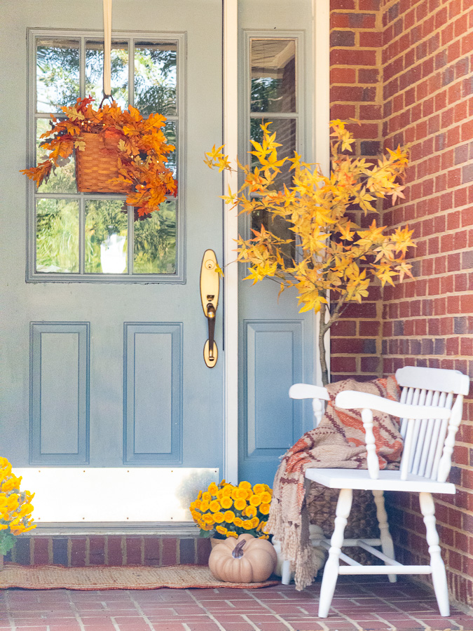 Brick porch with blue door decorated for fall.