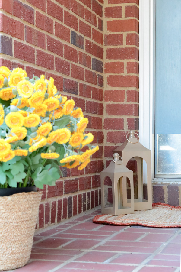 Two gold lanters from Dollar Tree in the corner of a brick porch