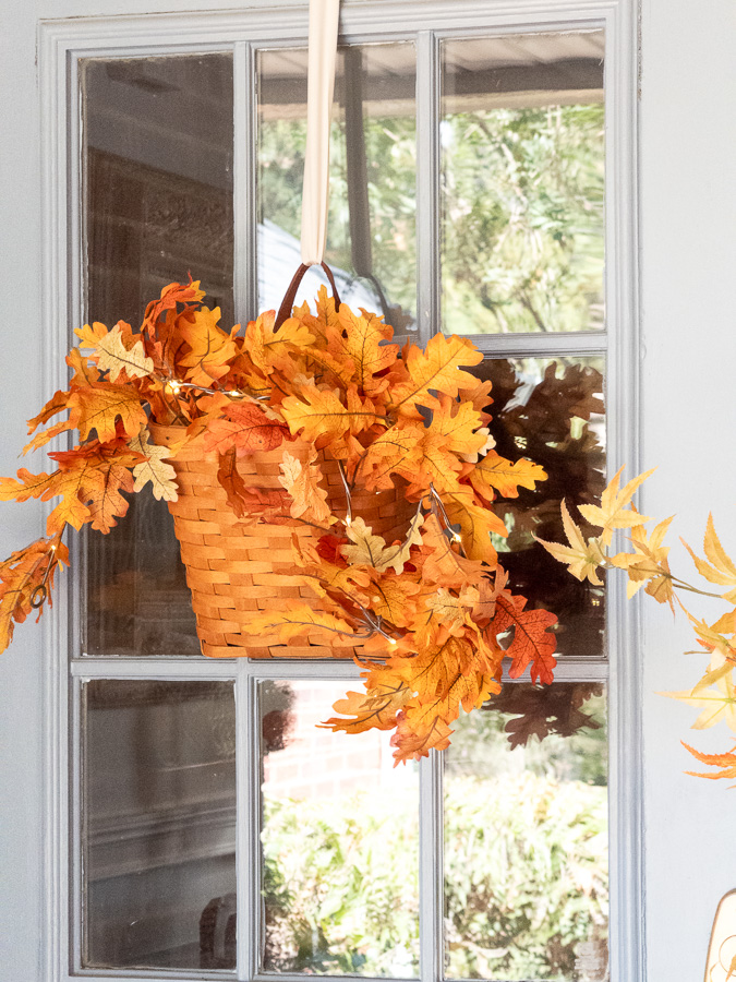 Longaberger basket hanging on a blue door filled with autumn leaf garland.