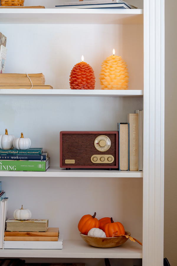 Wooden bowl filled with mini faux pumpkins on bottom shelf.  White mini pumpkins sitting on books and a vintage style radio