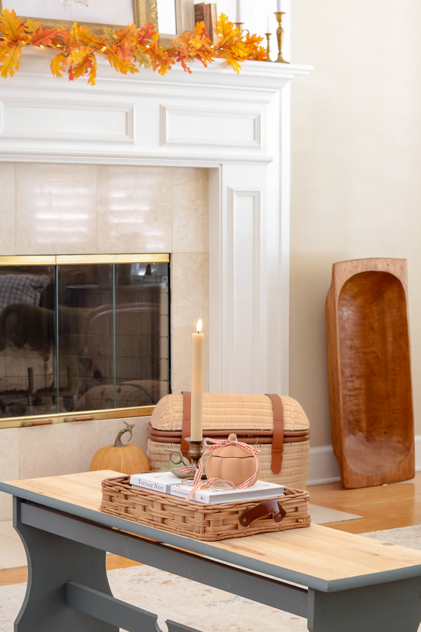 Blue wood bench acting as a coffee table with basket tray filled with white books including Vintage Nest.  Terracotta pumpkin jar on top of books and cnadle.