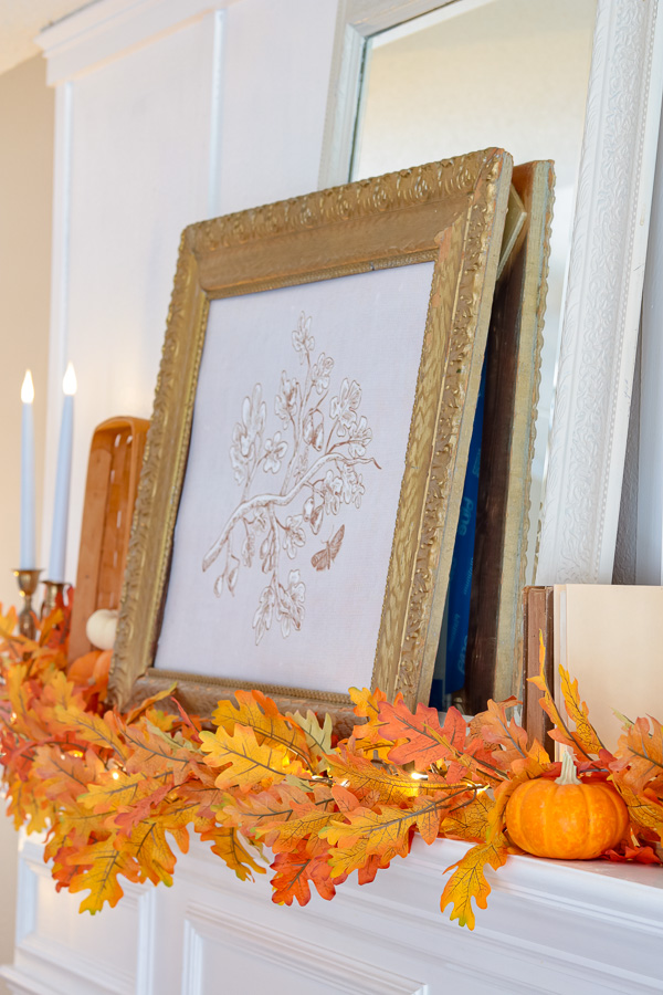 Oak branch and moth printable art autumn decorations framed in a vintage antique gold frame.  Orange fall leaf garland across mantel with mini pumpkins tucked in
