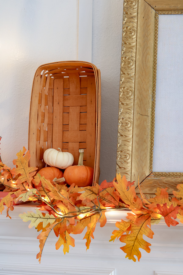 Basket filled with mini pumpkins and autumn leaf garland in front.