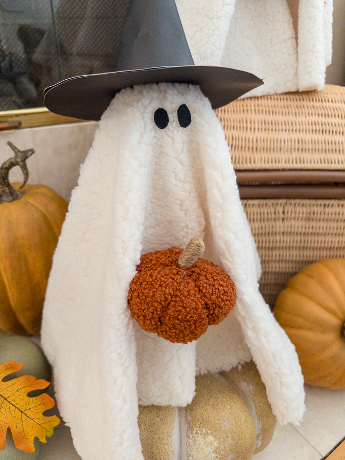 Soft sherpa ghost plush with black eyes and a friendly smile on a rustic table.