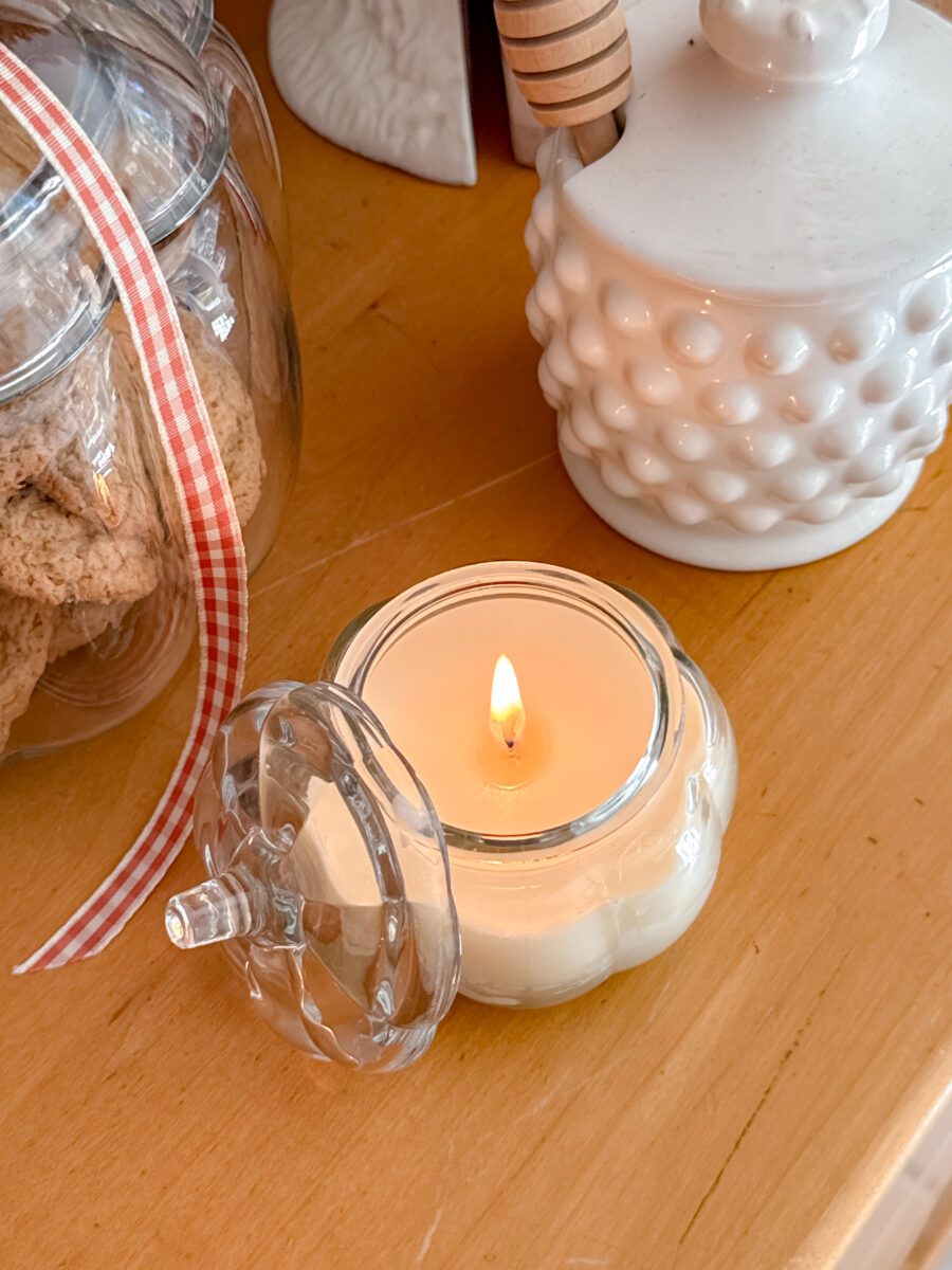 Beeswax candle lite on a wood hutch with other decorations around it.