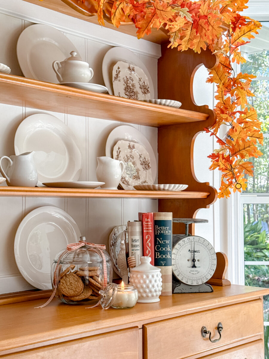 Beeswax candle lite on a wood hutch with other decorations around it.