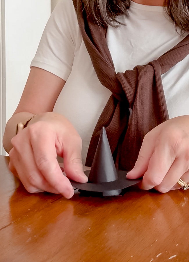Attaching the cone to the round brim with glue to finish the tiny paper witch hat.