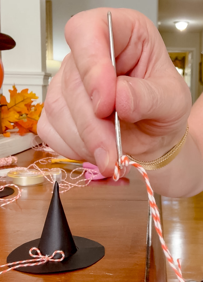 Threading twine through the top of the paper witch hat to create a loop for hanging the garland.