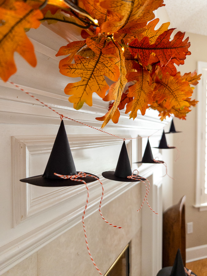Mini paper witch hat garland on a fireplace mantel for Halloween.