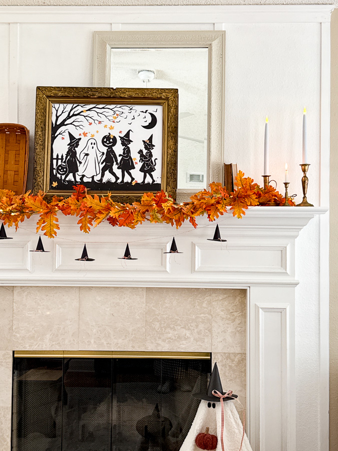 Fireplace mantel decorated for Halloween with trick or treat silhouette art, autumn leaf garland and mini paper witch hat garland
