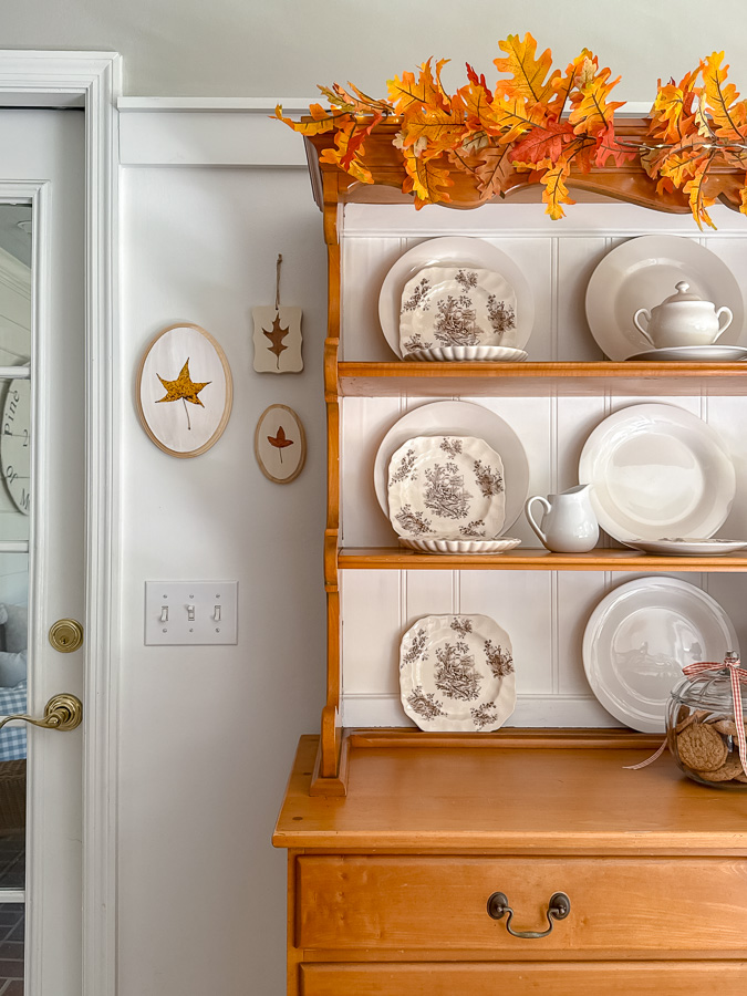 Preserved leaf art on wall next to a hutch that is decorated for fall.