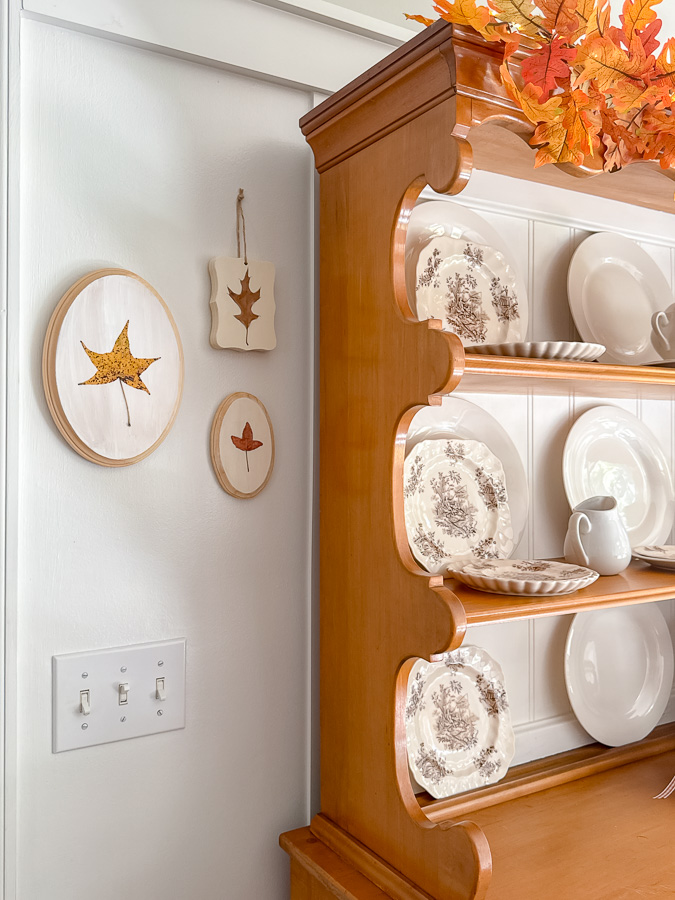 Hutch decorated for fall and next to hutch on wall is preserved leaf art.