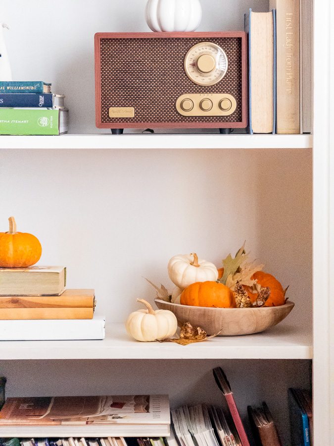 Wax preserved leaves in a wood bowl with real mini pumpkins on a bookcase with other decoration.