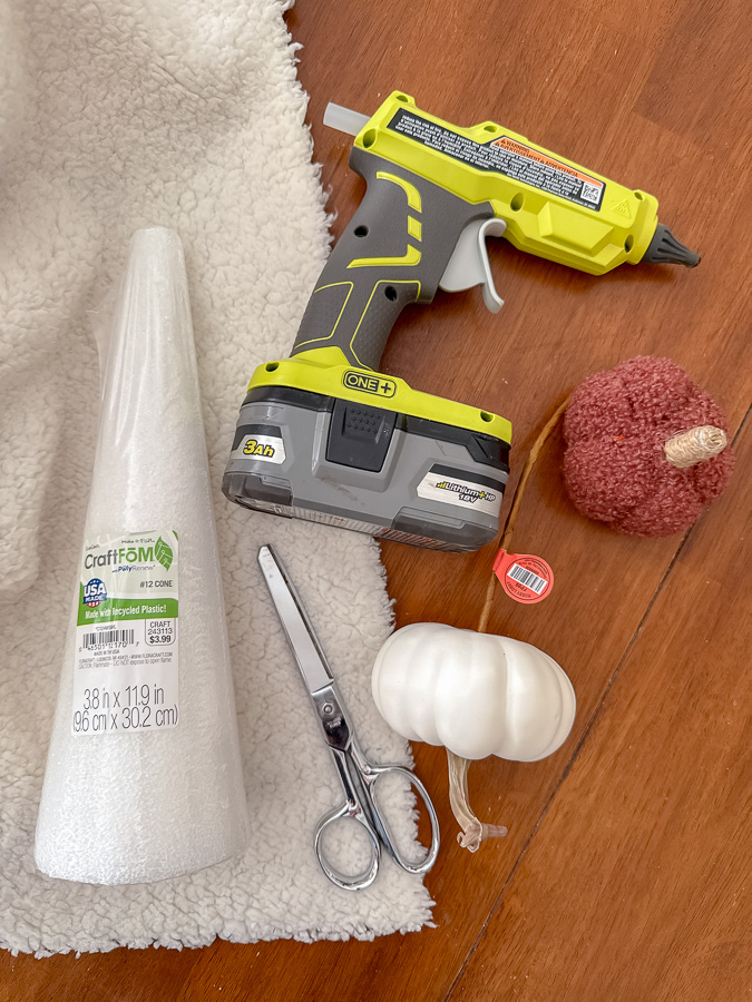 Supplies to make a sherpa ghost including sherpa fabric, scissors, styrofoam cone, mini pumpkins, glue gun, and black fel.