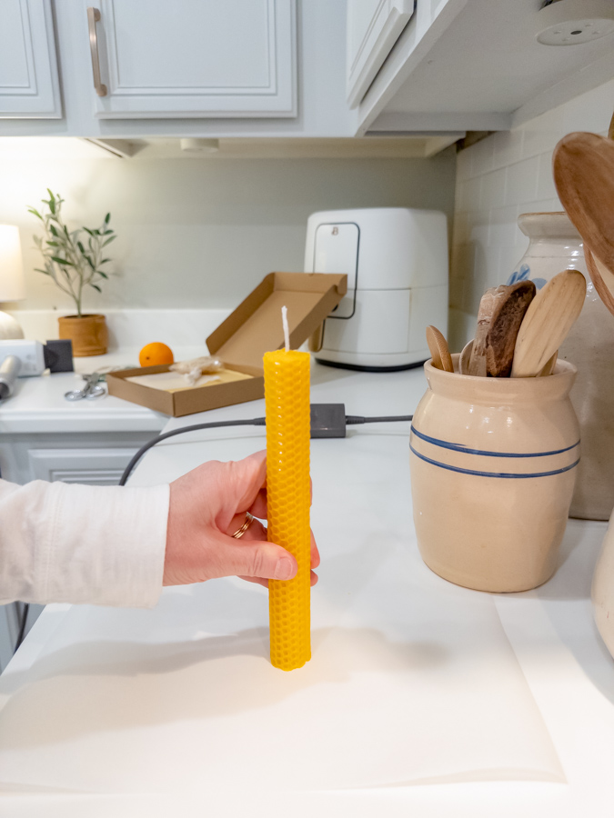 Standing a beeswax taper candle up on a countertop in a kitchen