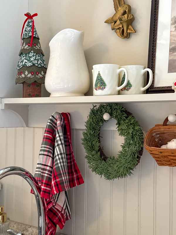 Ralph Lauren style decorations in a kitchen.  Felt Christmas tree, white vintage pitcher, Christmas tree mugs, wreath and plaid kitchen towel.