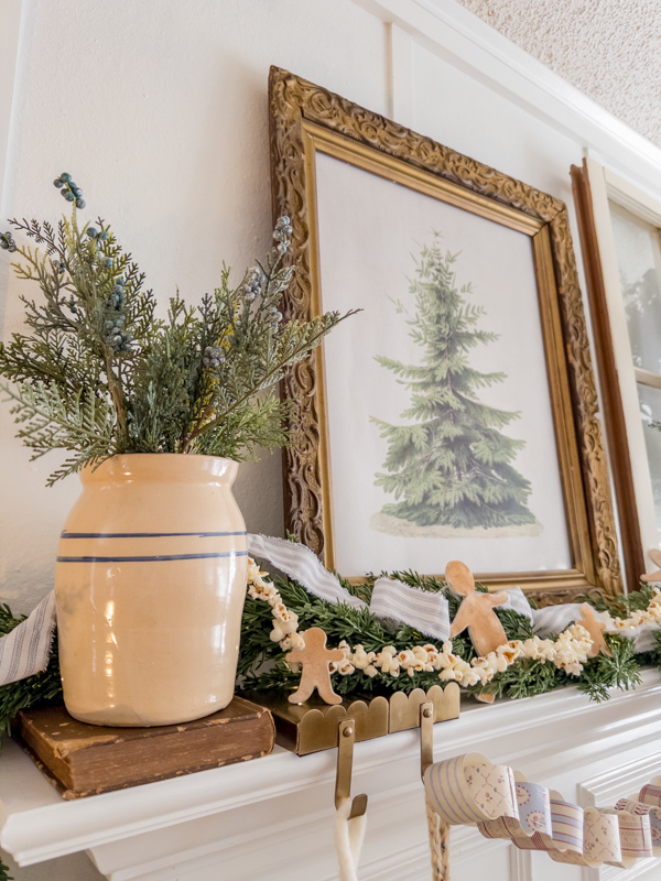 Botancial printable art in a vintage frame, greenery garland, ticking ribbon, popcorn garland and gingerbread men cookies, books, crock with greenery on a fireplace mantel. Inspired by Little House on the Prairie.