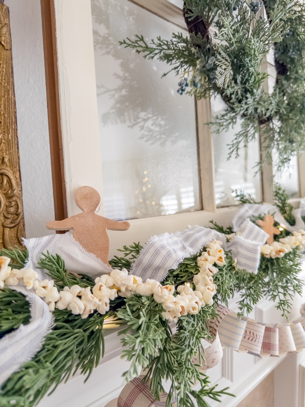 Fireplace mantel decorated with garland, ticking ribbon, popcorn and gingerbread cookies made of air dry clay. Modern prairie Christmas decor ideas.