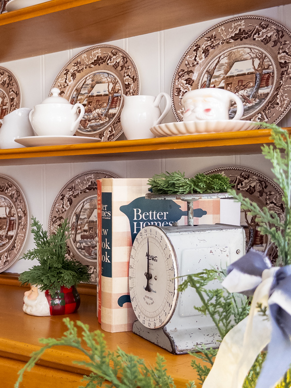 Hutch decorated for Christmas with brown and blue Currier and Ives style dishes and vintage Santa mugs, old scale and vintage cookbooks