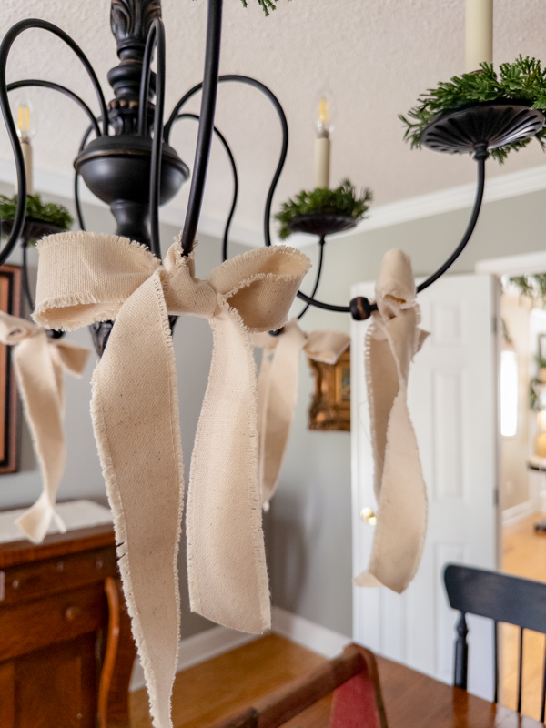 Off white cotton bows hanging on chandelier with greenery