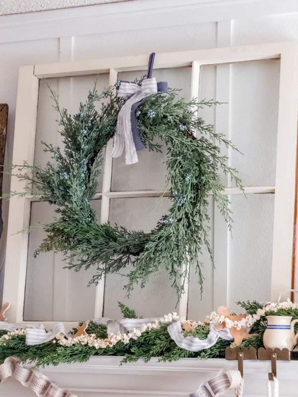 Modern prairie Christmas decor ideas. Mantel decorated for Christmas with an old window, greenery wreath and ticking bow.