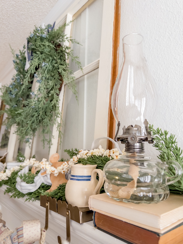 Old chamber lamp, greenery garland, popcorn garland, gingerbread men cookies, ticking ribbon and old books on a mantel inspired by a modern prairie look.