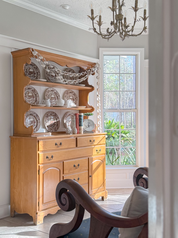 Hutch decorated for winter with old winter scene dishes Currier & Ives in browns and blues. And a cozy cottage pattern paper chain garland draped across the hutch.