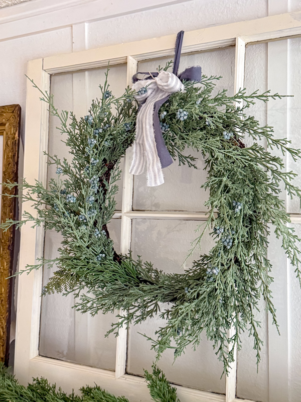 Old window with cedar wreath with a blue and white stripe ribbon