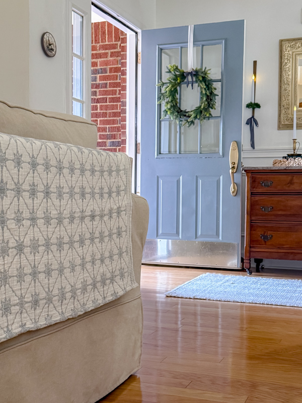 Easy transiton Christmas to winter decor using blankets like this one on the back of a sofa. And in the background is a blue door with a greenery wreath on it