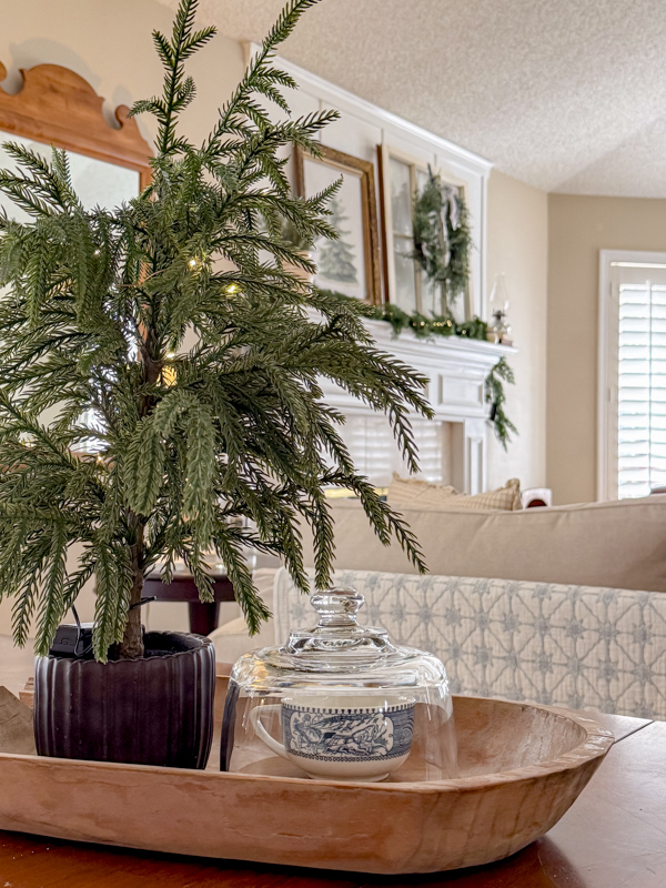 Library table centerpiece for winter. Wood dough bowl tray, small tree, cloche with a Currier & Ives teacup inside