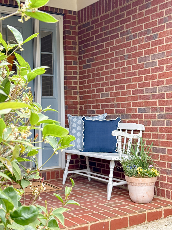 Elegant southern patriotic porch decor with white bench with blue pillows, container garden with an American flag in it and blue door.