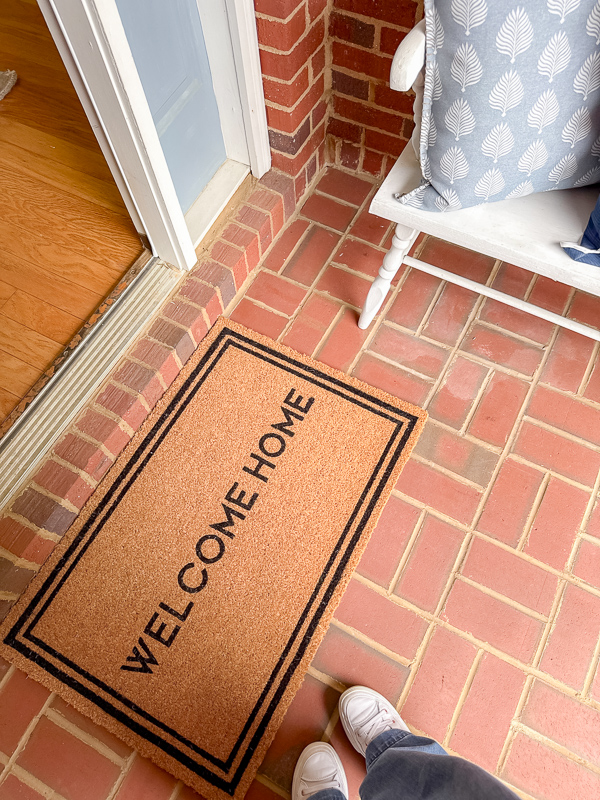 Natural fiber doormat placed on a clean brick porch floor for a simple spring entryway refresh.