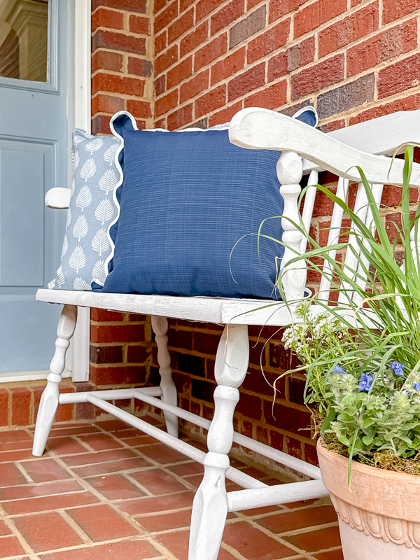 White vintage bench styled with allen + roth blue and white outdoor pillows from Lowe's for a spring porch refresh.
