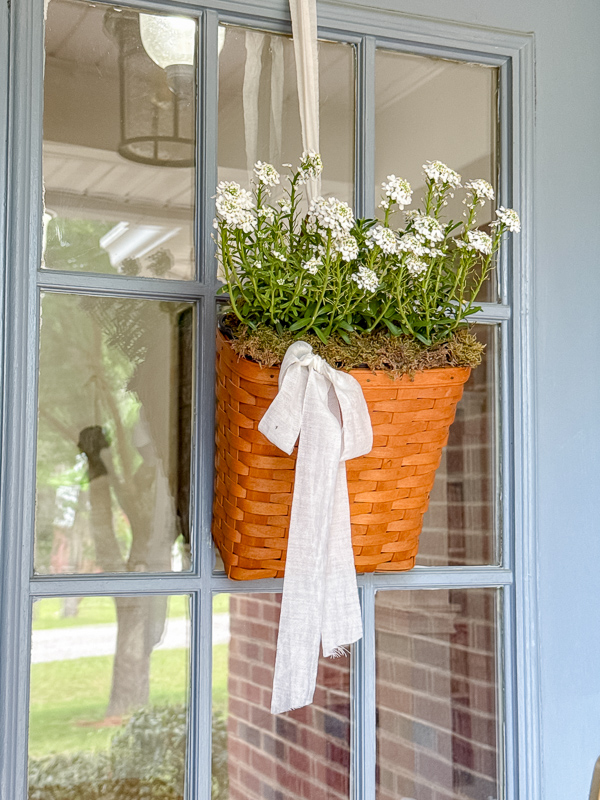 Vintage Longaberger basket hung on blue front door with white Snowsurfer Forte Candytuft flowers and an off-white ribbon.