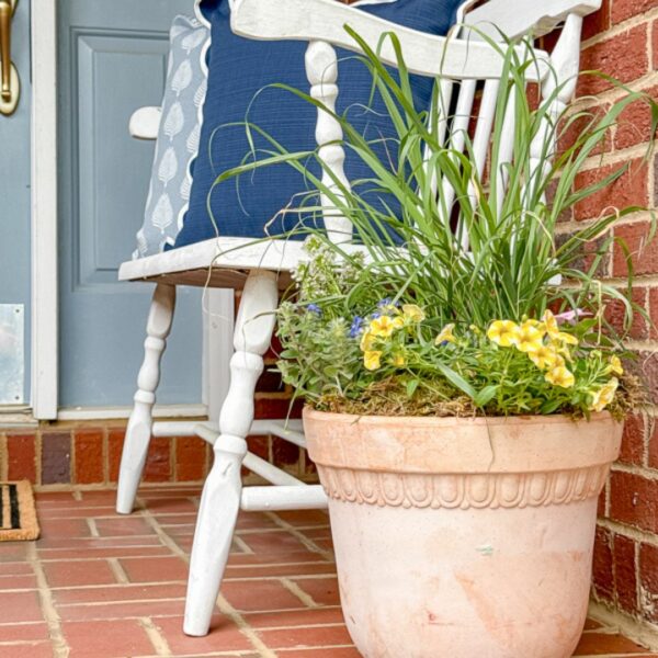 Simple spring porch refresh. Terracotta planter with flower garden, white bench and outdoor pillows all by Lowes