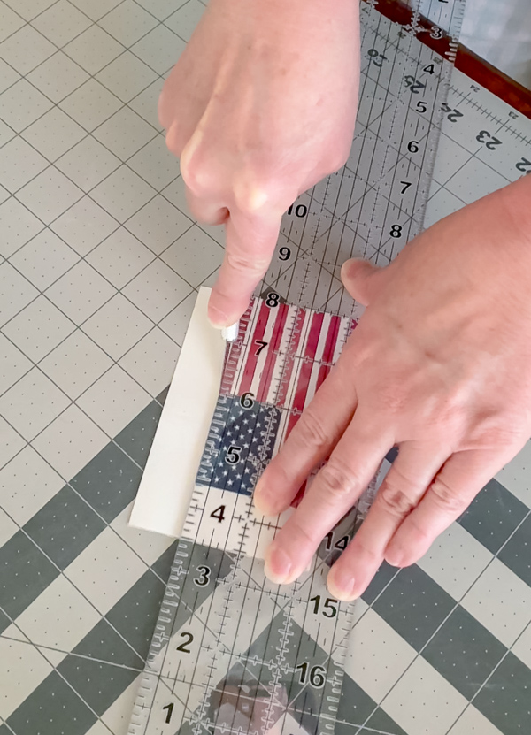 Cutting out a printed American flag on watercolor canvas paper using an X-ACTO knife and clear ruler on a cutting mat for clean straight edges