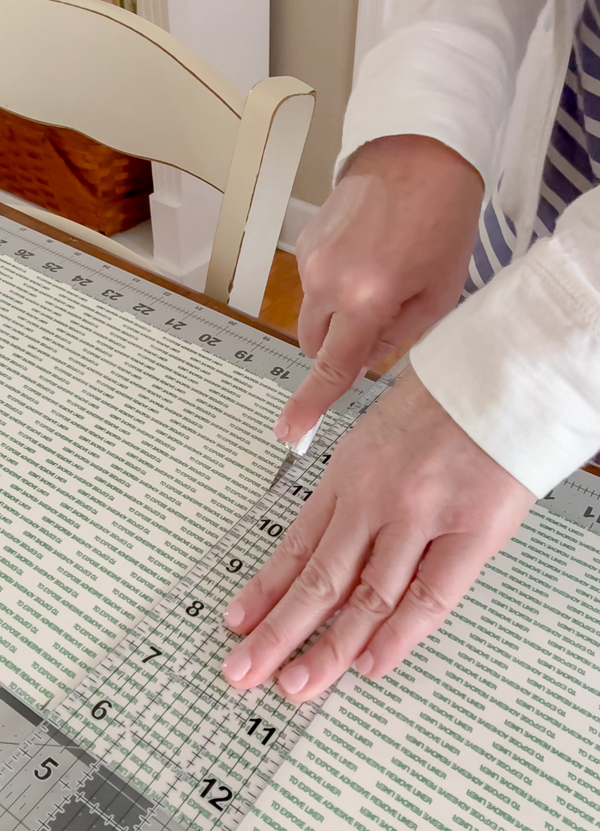 Cutting peel and stick foam board to size with an X-ACTO knife and clear ruler for DIY framed American flag art project