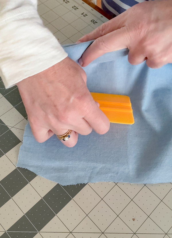 Using a squeegee to smooth chambray fabric onto peel and stick foam board to create a fabric background for DIY framed American flag art