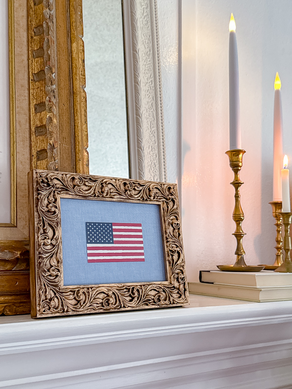 DIY framed American flag art on a fireplace mantel styled with brass candlesticks and a vintage gold mirror for patriotic home decor