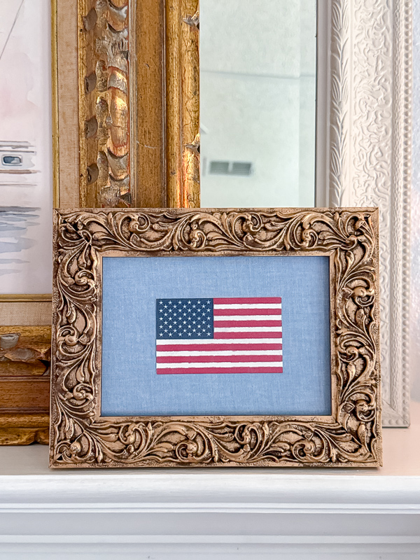 Framed canvas printed flag on a chambray background inside of an ornate gold frame.