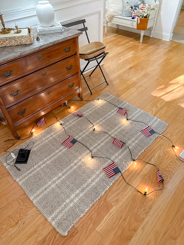 DIY American flag string light garland laid out on floor with solar panel and remote control before hanging