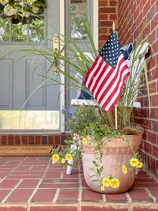 Terra cotta post with lemon grass for height and trailing flower around it and a medium size stick American flag sitting inisde the pot.