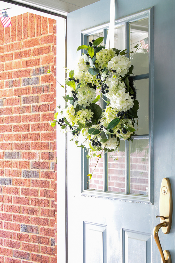 Beautiful southern style white and green hydrangea wreath with blue berries hanging on a blue front door.