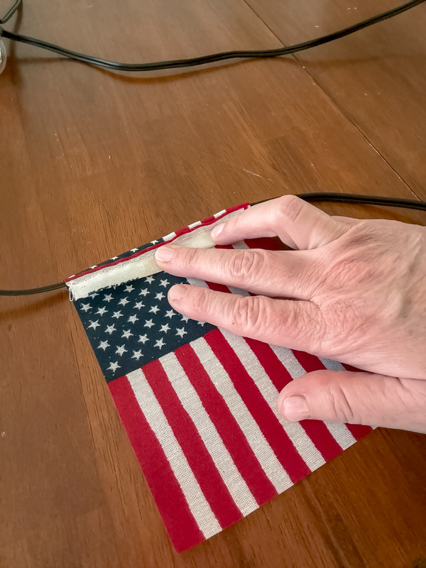 Folding the top of a stick American flag over outdoor string light wire for a DIY patriotic garland