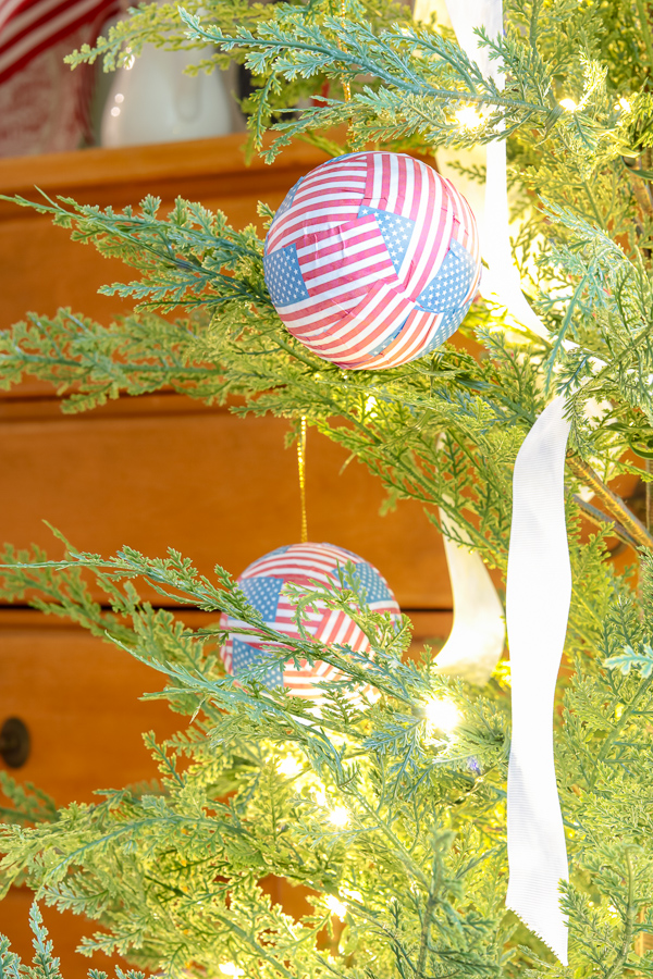 Mini paper American flags decoupaged to ball ornaments hanging on a christmas tree